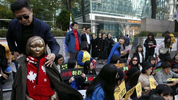 An activist puts his coat around the shoulders of the statue symbolising women and girls forced into sex slavery by the Japanese. The statue was placed outside the Japanese embassy in Seoul   in 2011. Photo: Woohae Cho