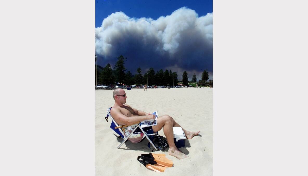 A man relaxes on Austinmer Beach, near Wollongong, as a bushfire rages in the background. Photo: GREG TOTMAN